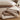 A folded beige bedding set with a matching pillowcase, featuring a small embroidered leaf pattern, styled on a wooden surface with a plush toy in the background.